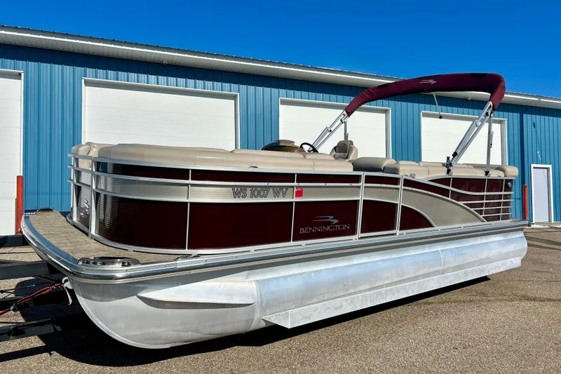 Slide: The Image of 2016 Bennington R21 pontoon boat with maroon and beige design, parked near blue building. - 25
