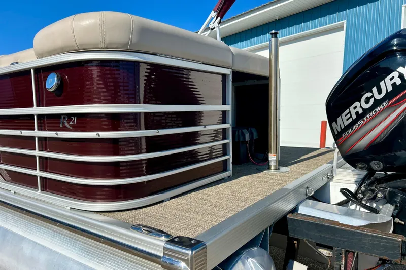 Slide: The Image of 2016 Bennington R21 pontoon boat with Mercury outboard motor, docked near a blue building. - 31