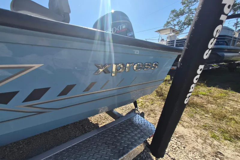 Slide: The Image of 2026 Xpress H20B Bay boat with metallic logo, parked outdoors in sunlight. - 13