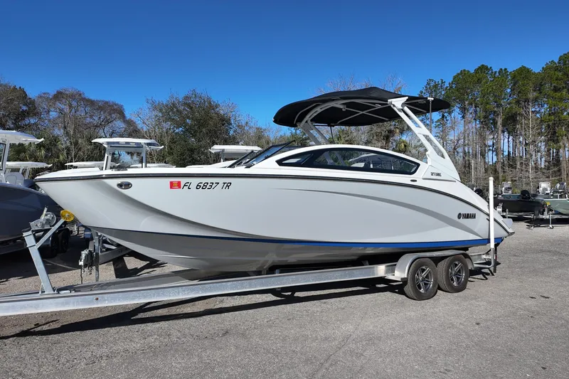 The Image of 2024 Yamaha Boats 275SE on trailer, sleek design, parked outdoors under clear blue sky. - 0
