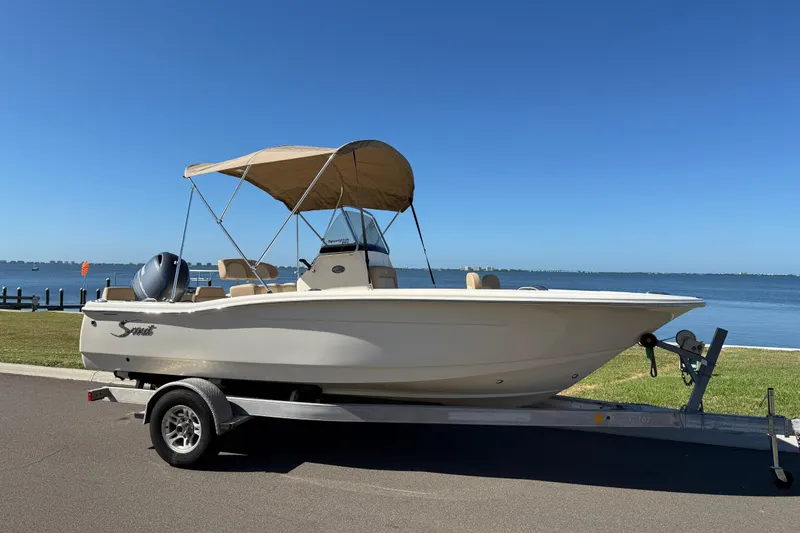 The Image of 2026 Scout 195 Sportfish boat on trailer by waterfront, featuring a canopy. - 0