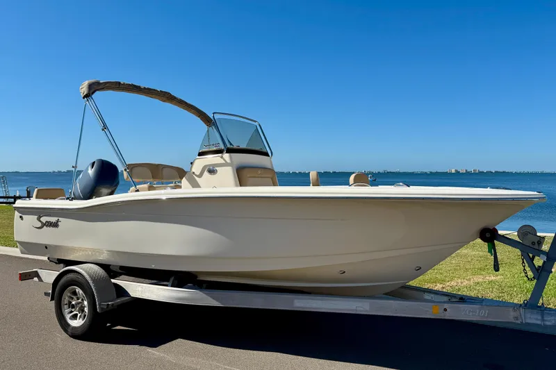 Slide: The Image of 2026 Scout 195 Sportfish boat on trailer by waterfront, clear blue sky. - 2