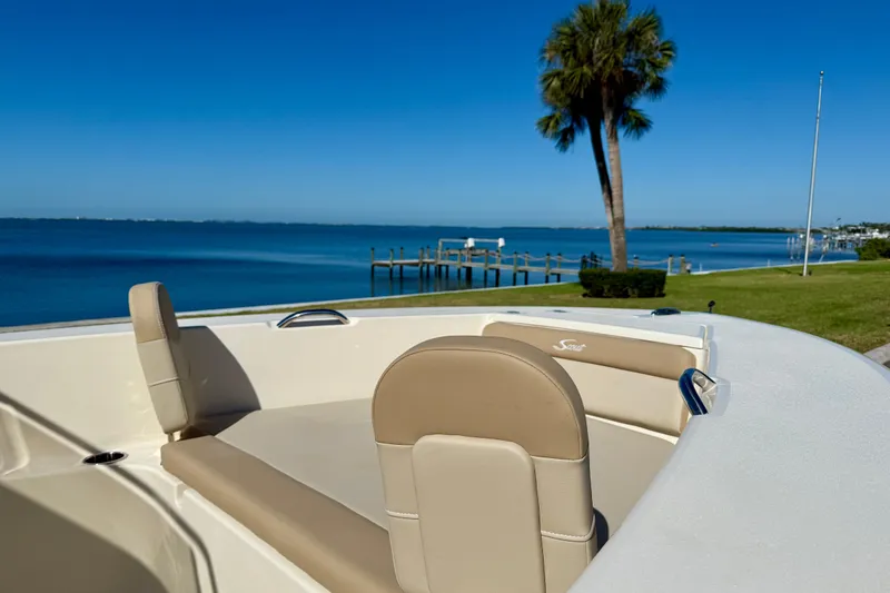 Slide: The Image of 2026 Scout 195 Sportfish boat with beige seating, overlooking serene waterfront and palm tree. - 25