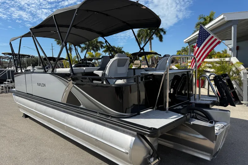Slide: The Image of 2026 Avalon 2385 LSZ Rear Fish Tri Toon boat with American flag, parked outdoors. - 8
