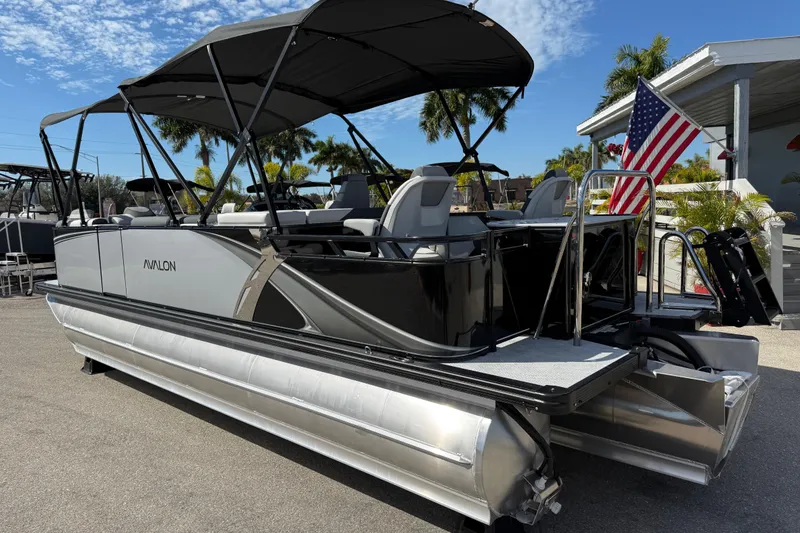 Slide: The Image of 2026 Avalon 2385 LSZ Rear Fish Tri Toon boat with American flag, parked outdoors. - 9
