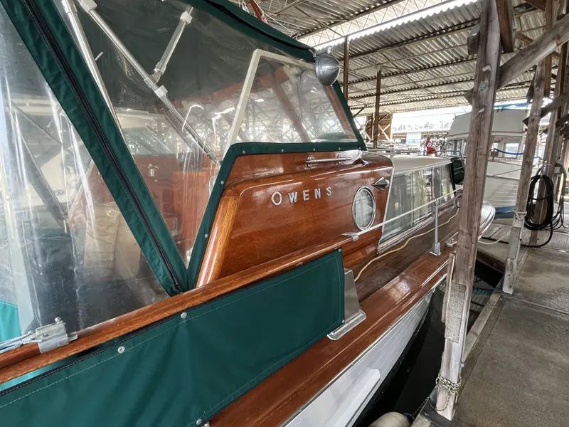 Slide: The Image of 1959 Owens Cabin boat docked, featuring wood finish and green cover. - 7