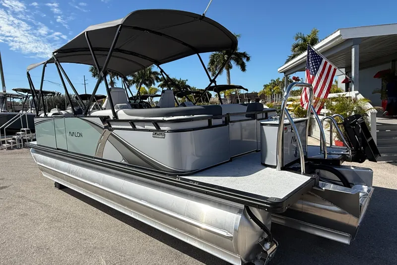 Slide: The Image of 2026 Avalon 2385 LSZ Quad Lounger Tri Toon boat with American flag, parked outdoors. - 8