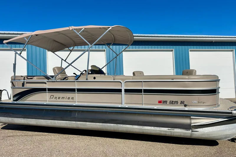 Slide: The Image of 2007 Premier 250 Intrigue pontoon boat with canopy, parked near blue storage units. - 2