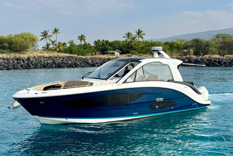 The Image of 2022 Sea Ray Sundancer 370 Outboard cruising in clear blue waters near a rocky shoreline. - 1