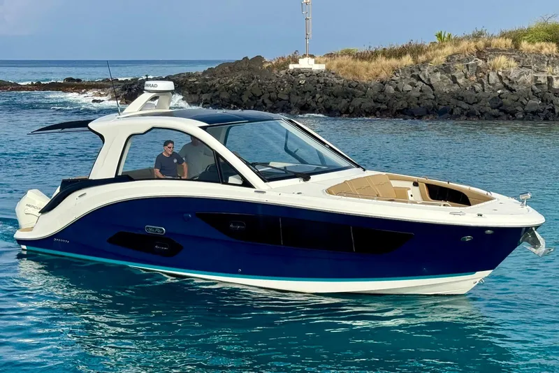 Slide: The Image of 2022 Sea Ray Sundancer 370 Outboard cruising in clear blue waters near rocky shoreline. - 6