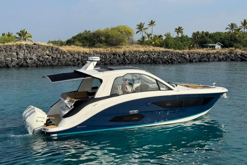 Slide: The Image of 2022 Sea Ray Sundancer 370 Outboard cruising in clear blue water near rocky shoreline. - 7