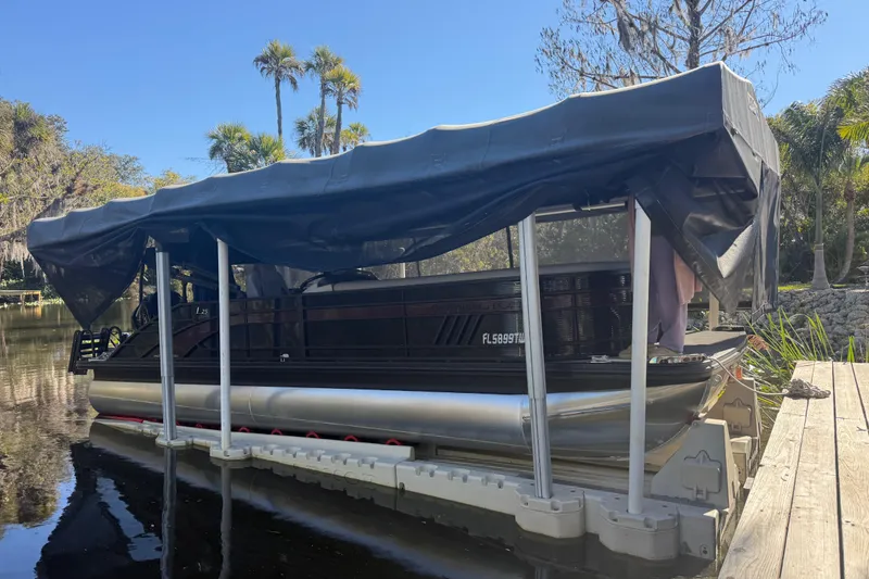 The Image of 2024 Bennington L Line pontoon boat docked with canopy, surrounded by lush greenery. - 0