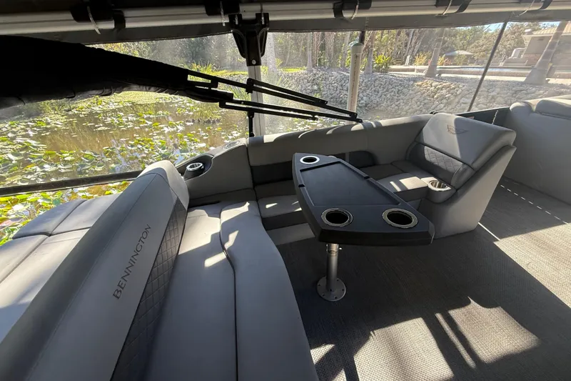 Slide: The Image of 2024 Bennington L Line boat interior with seating and table, overlooking a serene pond. - 10