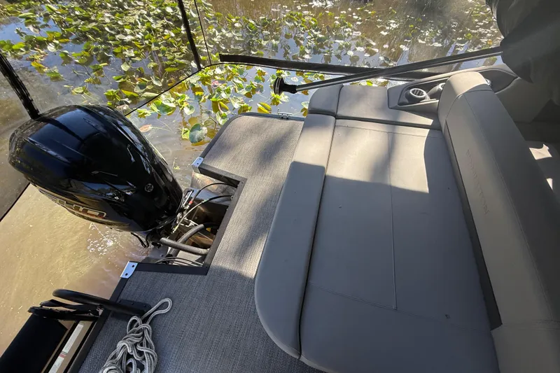 Slide: The Image of 2024 Bennington L Line boat interior with motor and seating, surrounded by water and plants. - 13