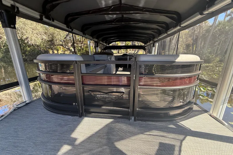 Slide: The Image of 2024 Bennington L Line pontoon boat with covered seating area on a calm waterway. - 4