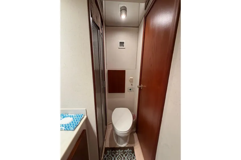 Slide: The Image of 1985 Bertram 54 Convertible yacht bathroom with toilet, wooden door, and patterned rug. - 39