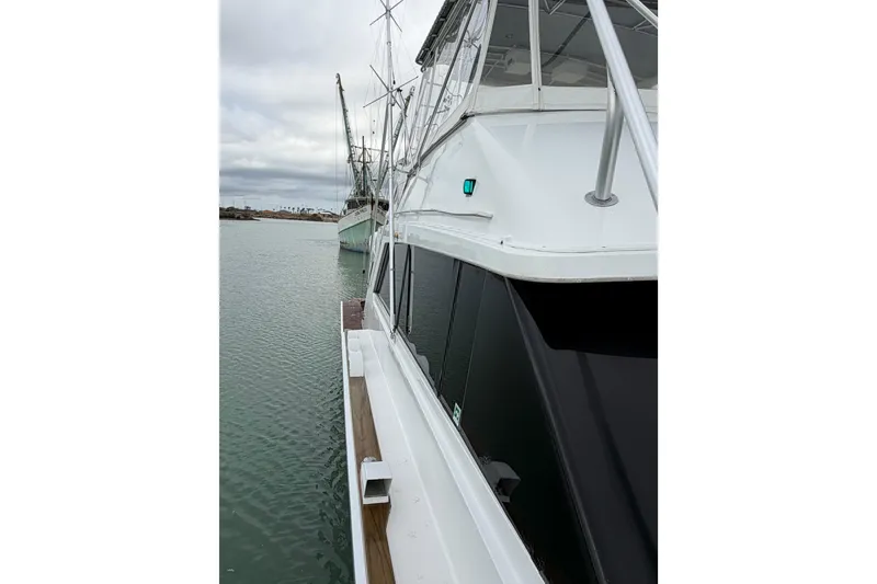 Slide: The Image of 1985 Bertram 54 Convertible yacht docked on calm water under cloudy skies. - 5