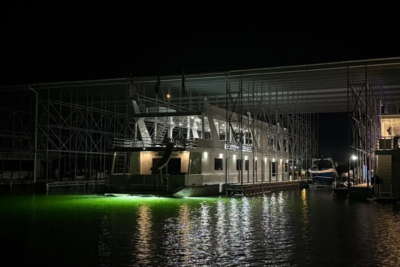 Slide: The Image of 2022 Trifecta HOUSEBOAT illuminated at night, docked under a large structure. - 11