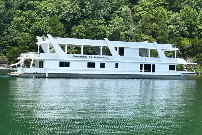 Slide: The Image of 2022 Trifecta HOUSEBOAT on a serene lake, surrounded by lush green trees. - 2