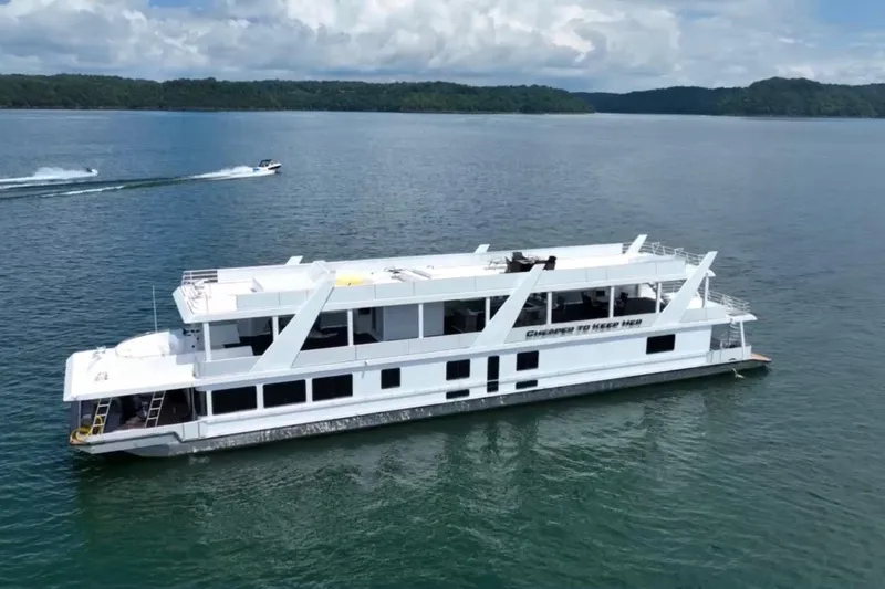 Slide: The Image of 2022 Trifecta HOUSEBOAT cruising on a serene lake with lush green hills. - 4