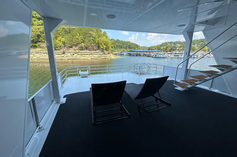 Slide: The Image of 2022 Trifecta houseboat deck with chairs, overlooking serene lake and lush greenery. - 43