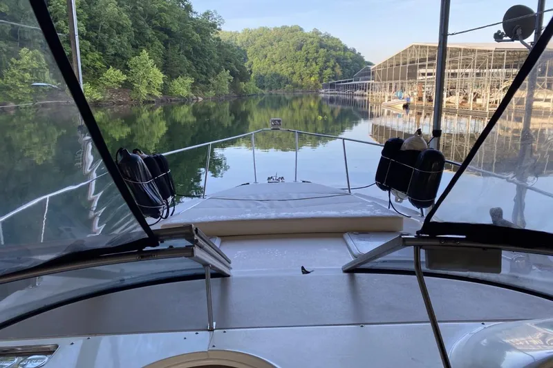 Slide: The Image of 2004 Larson Cabrio 330 boat on calm lake near marina and lush greenery. - 1