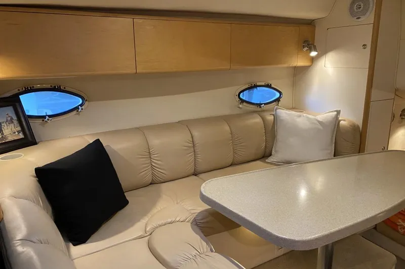 Slide: The Image of 2004 Larson Cabrio 330 interior with beige seating, table, and porthole windows. - 8
