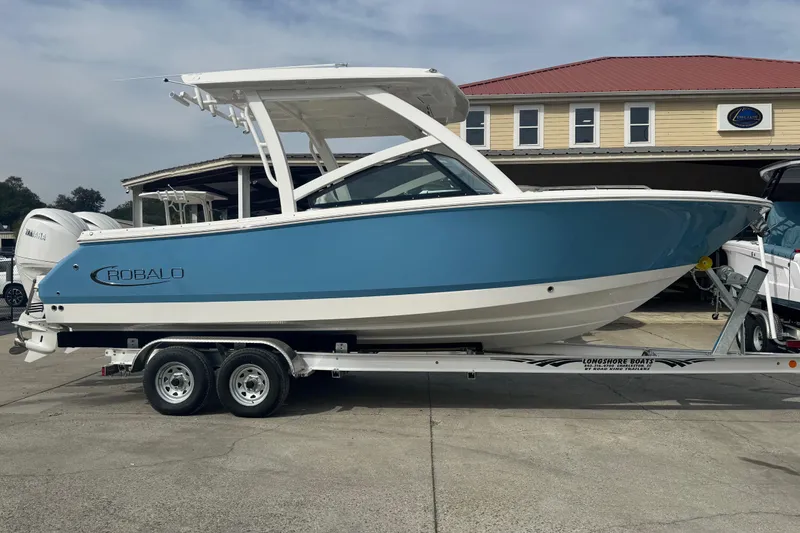 The Image of 2026 Robalo R257 Dual Console boat on trailer, blue and white design. - 0