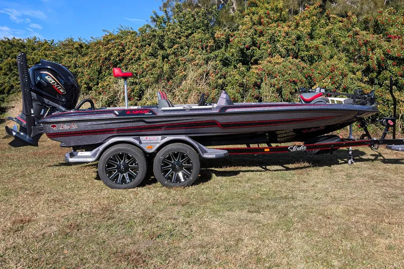 Slide: The Image of 2026 Bass Cat Lynx STS boat on trailer, parked on grass with trees in background. - 2