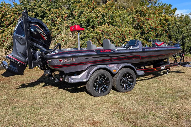 Slide: The Image of 2026 Bass Cat Lynx STS boat on trailer, parked on grass with lush greenery background. - 3