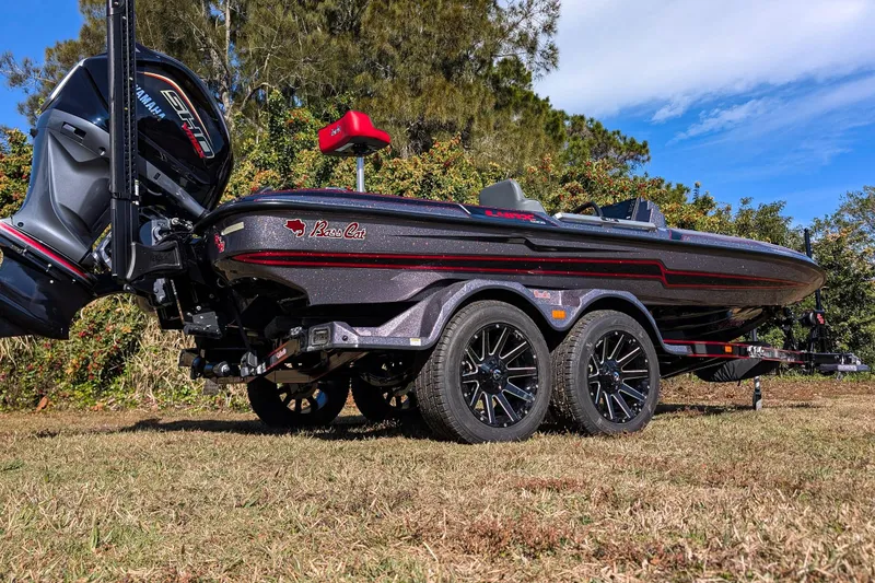 Slide: The Image of 2026 Bass Cat Lynx STS boat on trailer, parked on grass with trees in background. - 6