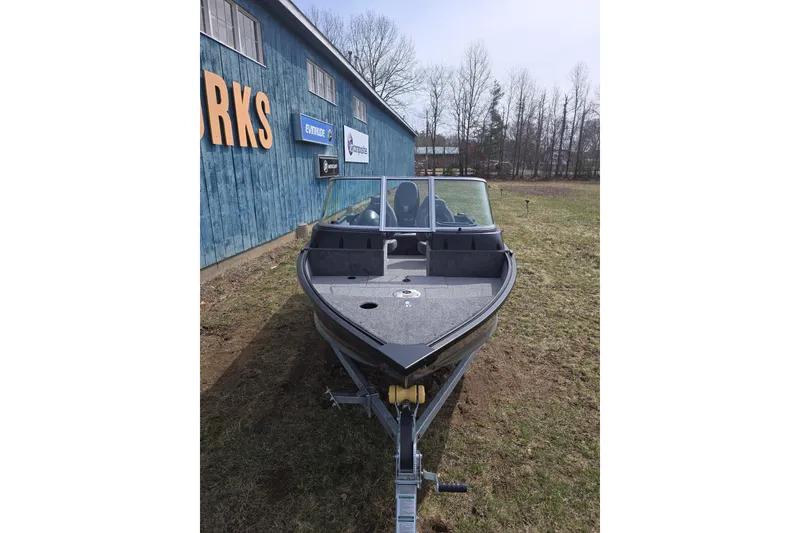 Slide: The Image of 2026 Alumacraft Classic 165 Sport boat on trailer, parked outdoors near a blue building. - 4