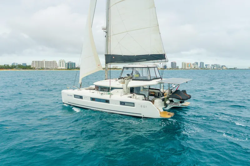 Slide: The Image of 2024 Lagoon 51 catamaran sailing near a coastal city skyline. - 93