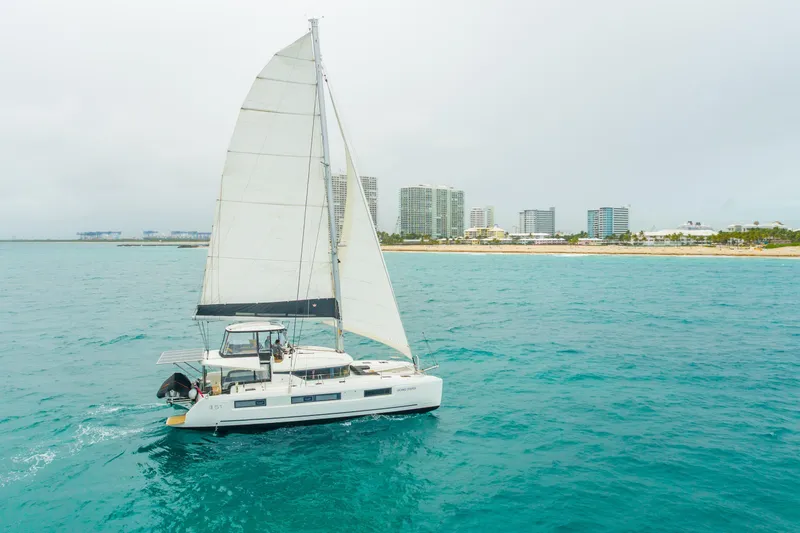 Slide: The Image of 2024 Lagoon 51 sailing near a coastal city skyline on a cloudy day. - 95