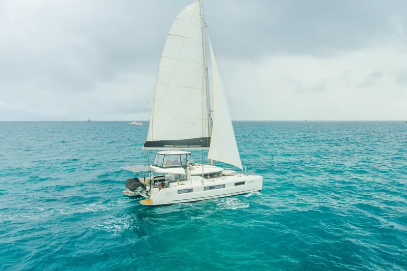 Slide: The Image of 2024 Lagoon 51 catamaran sailing near a coastal city skyline. - 96