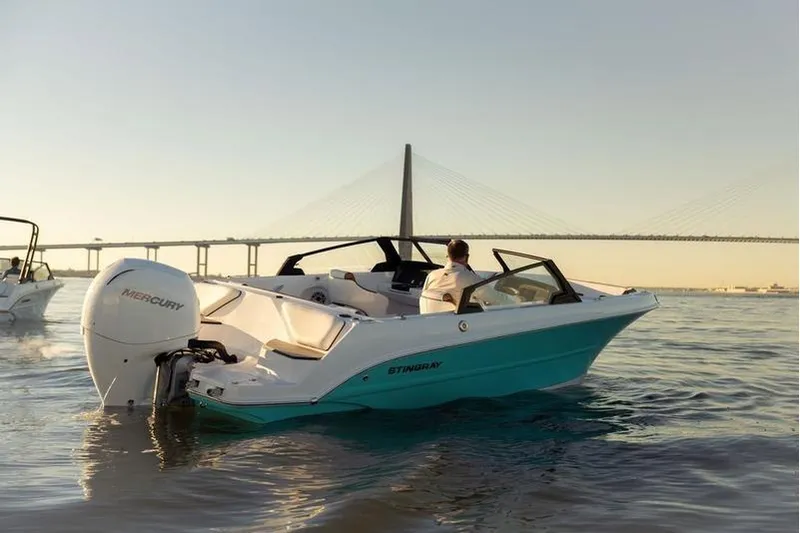 The Image of 2026 Stingray 20 SBX boat cruising near a bridge at sunset. - 0
