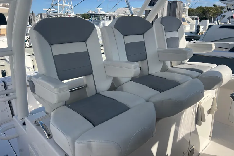 Slide: The Image of 2019 Pursuit S 368 Sport boat seats, featuring gray and white cushioned design at a marina. - 15