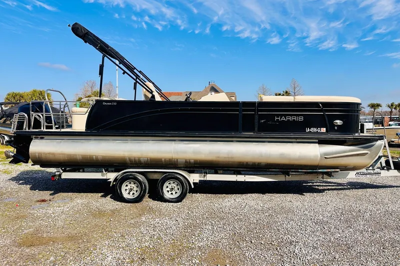 The Image of 2019 Harris Cruiser 250 pontoon boat on a trailer, parked outdoors under a clear blue sky. - 0