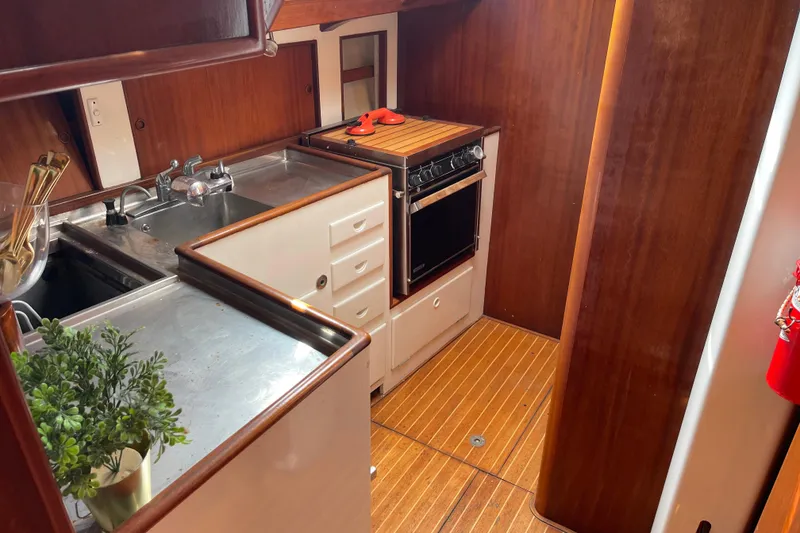 Slide: The Image of 1972 Rhodes 53 Motorsailor kitchen with wood cabinetry, stainless steel sink, and compact stove. - 67