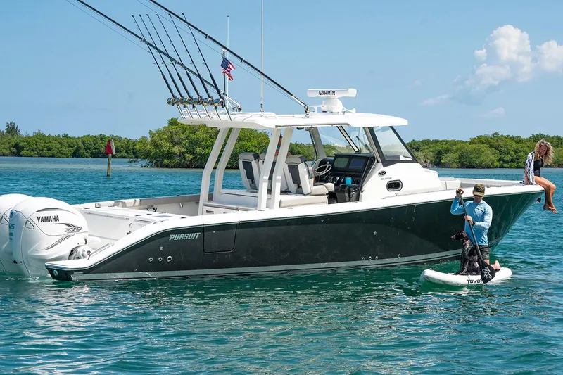 Slide: The Image of Manufacturer Provided Image: 2025 Pursuit S 358 Sport boat on water with fishing rods and paddleboarder nearby. - 3