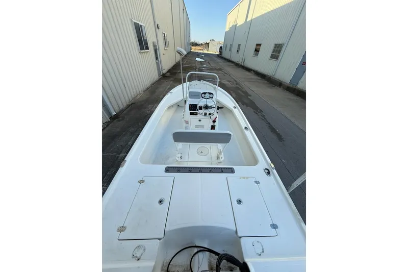 Slide: The Image of 2024 Mako 18 LTS boat, white deck, parked beside industrial building. - 2