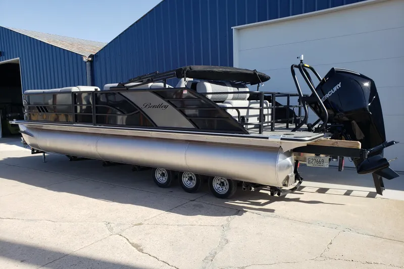 Slide: The Image of 2026 Bentley Pontoons Elite 253 Swingback Bench with Mercury engine, parked outside a blue building. - 3