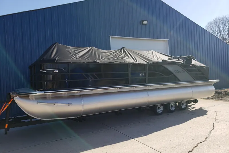 Slide: The Image of 2026 Bentley Pontoons Elite 253 Swingback Bench, covered, parked outside blue building. - 6