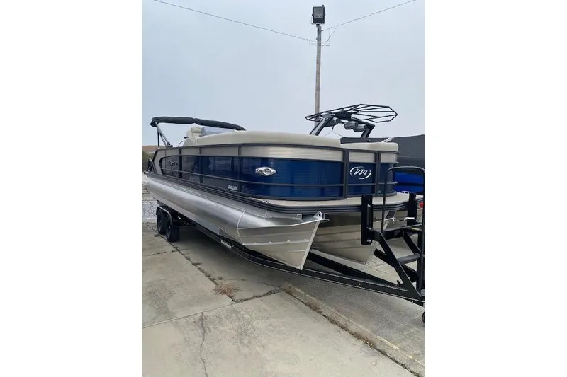 The Image of 2026 Manitou 25 Encore SL SHP pontoon boat on trailer, parked outdoors. - 1