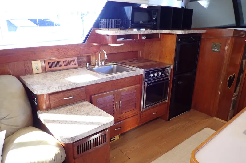 Slide: The Image of 1988 Mainship boat kitchen with wood cabinetry, sink, stove, microwave, and refrigerator. - 15