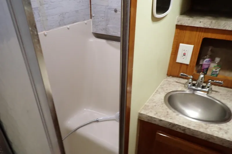 Slide: The Image of 1988 Mainship boat bathroom with shower, sink, and toiletries on a marble countertop. - 21