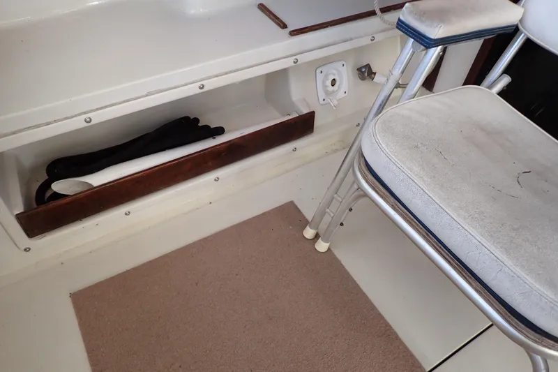 Slide: The Image of 1988 Mainship boat interior with storage compartment, folding chair, and carpeted floor. - 33