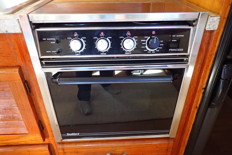 Slide: The Image of 1988 Mainship boat kitchen with Princess stove and oven, featuring wooden cabinetry. - 67