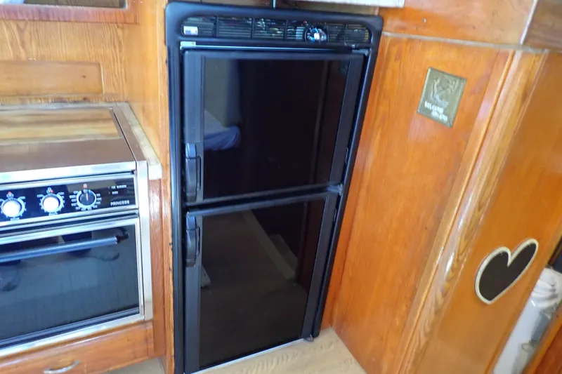 Slide: The Image of 1988 Mainship kitchen with black fridge and stainless steel oven, wooden cabinetry. - 69