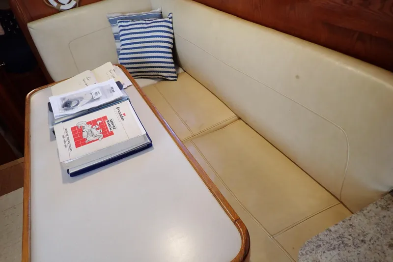 Slide: The Image of 1988 Mainship interior with beige seating, table, manuals, and striped pillow. - 75